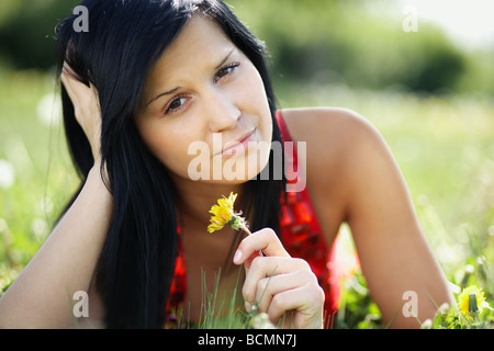 Bella donna giacente nel giardino tenendo un dente di leone Foto Stock