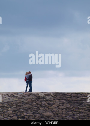 Coppia di mezza età in piedi sulla struttura di frangionde kissing Foto Stock