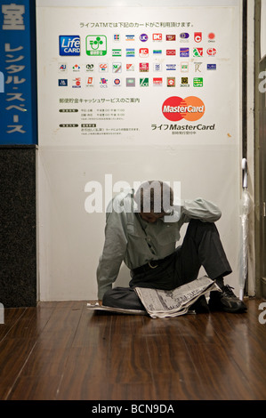 Un senzatetto leggendo un giornale in Shibuya distretto commerciale di Tokyo Giappone Foto Stock