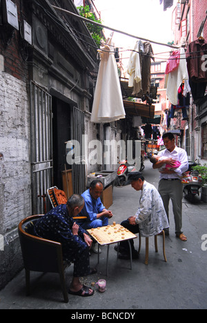 Anziani di Shanghai giocando a scacchi cinesi in un nongtang come un giovane padre holding bambino guarda sulla, Shanghai, Cina Foto Stock