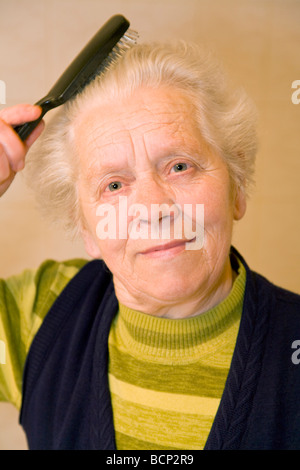 Frau in ihren Siebzigern bürstet sich ihre grauen Haare Foto Stock