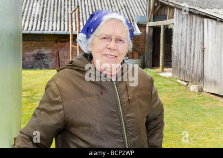 Frau in ihren Siebzigern mit Kopftuch posiert vor ihrem Bauernhof Foto Stock