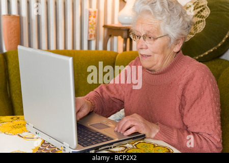 Frau in ihren Siebzigern sitzt im Wohnzimmer am Laptop Foto Stock