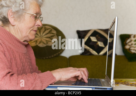 Frau in ihren Siebzigern sitzt im Wohnzimmer am Laptop Foto Stock