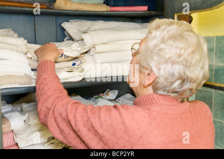 Frau in ihren Siebzigern steht vor einem geöffneten Wäscheschrank und schaut die Textilien un Foto Stock