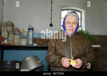 Frau in ihren Siebzigern mit Kopftuch sitzt in der Waschküche und schält sich einen Apfel Foto Stock