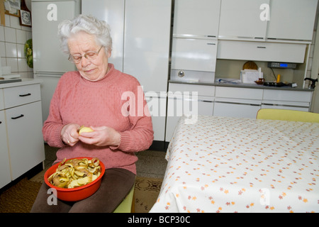 Frau in ihren Siebzigern sitzt in der Küche und schält Kartoffeln Foto Stock