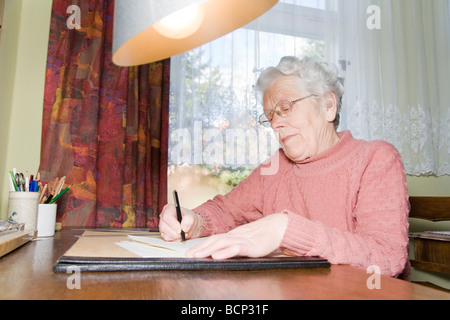 Frau in ihren Siebzigern sitzt am Schreibtisch und schreibt einen breve Foto Stock