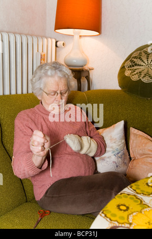 Frau in ihren Siebzigern sitzt im Wohnzimmer und stopft Wollsocken Foto Stock