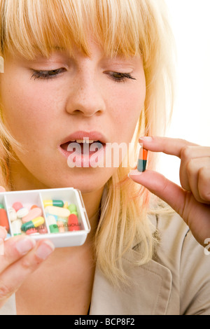 Junge Frau mit einer Pillendose in der schaut mano eine bunte Kapsel unsicher un Foto Stock