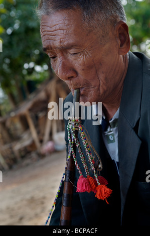 Vecchio Hmong hill tribe uomo riproduzione di un tradizionale strumento di bambù in un villaggio nel nord della Tailandia Foto Stock