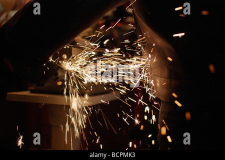 Un uomo che tiene in mano e utilizza la smerigliatrice angolare e le scintille vola in una fabbrica americana Stati Uniti primo piano orizzontale di alta risoluzione Foto Stock