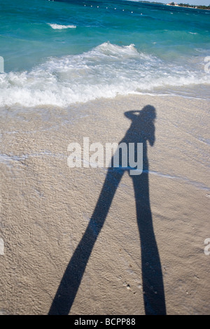 Una persona in possesso di una fotocamera e scattare una foto sulla spiaggia di sabbia di oro e blu brillante acqua Foto Stock