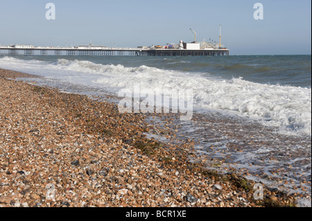 Spiaggia deserta con onde che si infrangono come marea entra in infront di divertimento pier a Brighton cittadina balneare Foto Stock