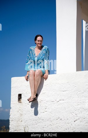 Donna in blu kaftan siede sul muro bianco in Grecia Foto Stock