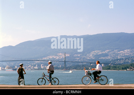 I ciclisti ciclismo su Stanley Park Seawall lungo Burrard ingresso affacciato sulla North Shore Mountains Vancouver British Columbia Canada Foto Stock