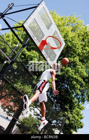 Bello sportivo americano africano uomo vestito di bianco di saltare in aria per raggiungere il cesto mentre giocare a basket dunk Foto Stock