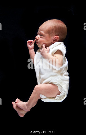Neonato boy raccolta il suo naso fotografato su un nero di sfondo per studio. Foto Stock