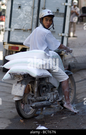 Giovane uomo a piedi nudi di trasportare sacchi di farina sulla sua moto in Cho Lon la Chinatown di Ho Chi Minh City Vietnam Foto Stock