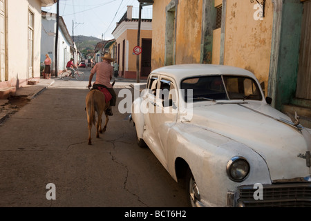 Strada in Trinidad, Cuba, uomo sul mulo passando vintage anni cinquanta auto Foto Stock