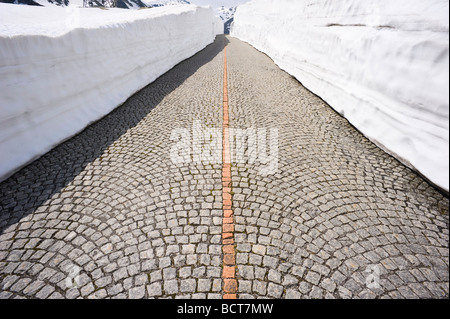 Pavimentazione in ciottoli della vecchia strada del San Gottardo tra alti muri di neve, Svizzera, Europa Foto Stock