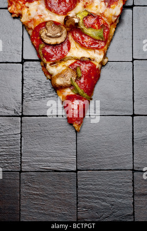 Un trancio di pizza su un nero lo sfondo di legno Foto Stock