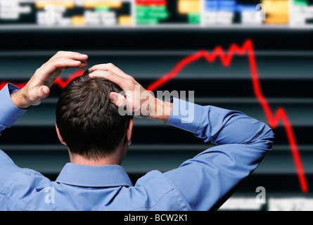 Stock Trader stringendo la sua testa davanti a una schermata che mostra un crash del mercato azionario Foto Stock