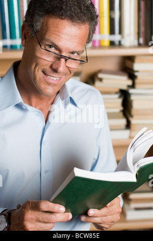 Uomo maturo la lettura di un libro in una libreria con un paio di occhiali Foto Stock