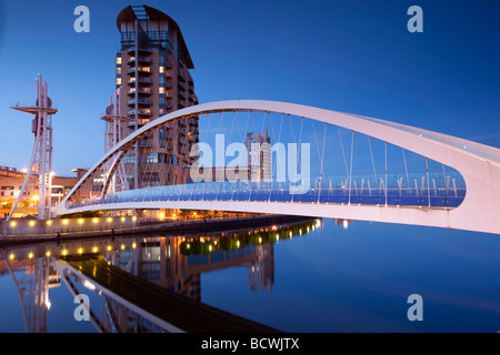 Un ponte pedonale a Salford Quays, Manchester visto al crepuscolo contro un cielo blu con le luci. Lowry Centre shopping. Foto Stock