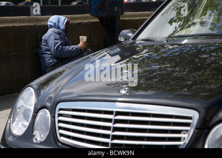 Uomo maschio street mendicante che giace accanto a un biglietti per il parcheggio della macchina e Mercedes vettura cercando di ricambio cambia città di Dublino che illustra la ricchezza disuguaglianza Foto Stock