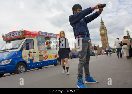 Un giovane uomo asiatico prende una fotografia da Westimnster Bridge, vicino al Big Ben mentre una bella giovane ragazza bionda mangia un gelato Foto Stock