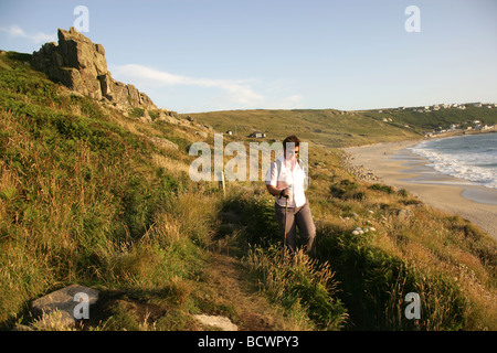 Area di Sennen, Inghilterra. Signora camminare da solo lungo il sentiero costiero con Sennen Cove in background. Foto Stock