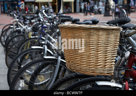 Fila di biciclette con un vecchio stile di shopping in vimini cesto in un bike park a Dublino Repubblica di Irlanda Foto Stock