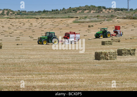 Trattori nel campo dell'imballaggio di paglia piccole balle di paglia in quelli più grandi al momento del raccolto Foto Stock