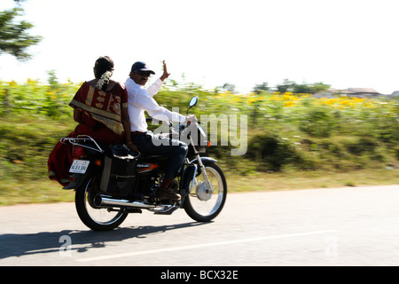 Un uomo aziona una moto e sua moglie si trova sulla parte posteriore della moto. Il panning viene usata per seguire il moto e tenerlo nel fuoco. Foto Stock