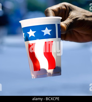 La mano della persona senza dimora, tenendo fuori bicchiere di carta con noi bandiera a mendicare per cambiare su Pennsylvania Avenue a Washington DC. Foto Stock