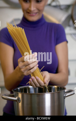 La donna in cucina mettendo gli spaghetti in padella Foto Stock