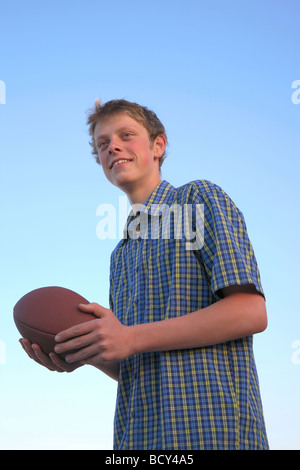 Ragazzo adolescente con un calcio americano pronto a lanciare contro un cielo blu al tramonto. Foto Stock