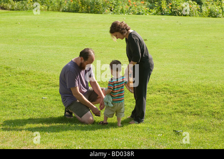 Famiglia di tre sull'erba assieme mettendo sui pattini del bambino di due anni Foto Stock