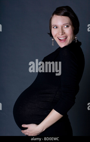 Donna incinta sorridente e tenendo la pancia, indossare un abito nero. Foto Stock