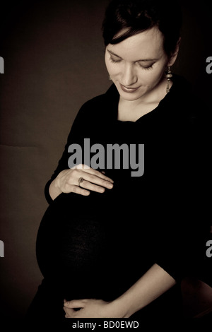 Donna incinta guardando in giù a pancia con la mano sulla parte superiore e inferiore Foto Stock
