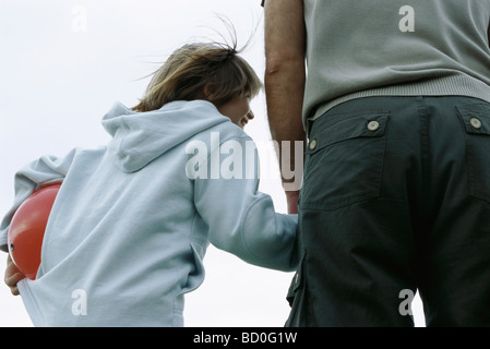 Giovane ragazzo ridendo, tenendo la mano del padre che porta palla sotto il braccio, vista posteriore Foto Stock