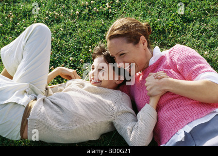 Madre e figlia reclinate in erba, ridere, tenendo le mani Foto Stock