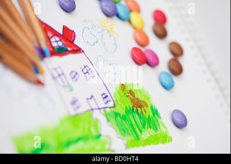 Bambino il disegno di una casa e il cane con matite colorate circondato da smarties Foto Stock