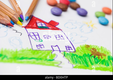 Bambino il disegno di una casa e il cane con matite colorate circondato da smarties Foto Stock