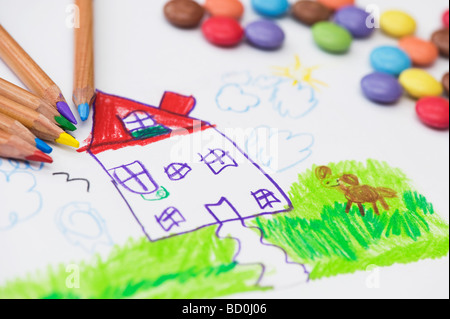 Bambino il disegno di una casa e il cane con matite colorate circondato da smarties Foto Stock