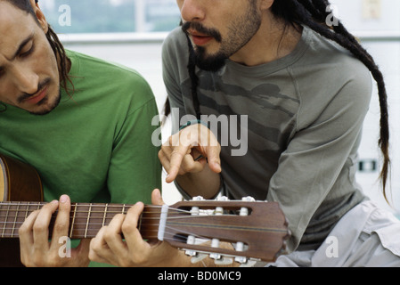 L'uomo insegnamento amico a giocare la chitarra acustica Foto Stock