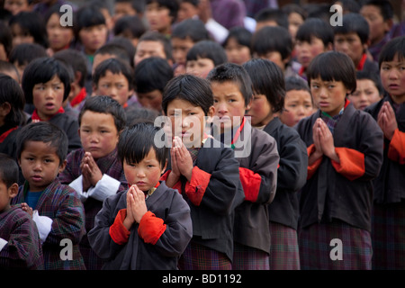 Un gruppo di giovani la scuola dei bambini in divisa rosso bracciali manicotti pregando in corrispondenza del gruppo nel parco giochi scuola 91948 Bhutan-Wangdue Foto Stock