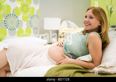 Donna incinta rilassante sul letto, sorridente Foto Stock