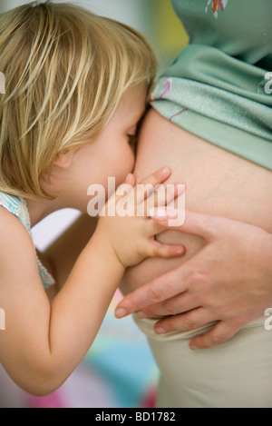Piccola ragazza baciare la madre del ventre in stato di gravidanza Foto Stock